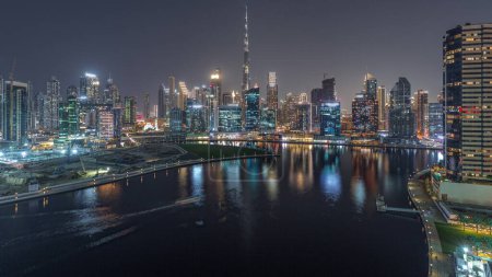 Téléchargez les photos : Vue panoramique aérienne sur Dubai Business Bay et le centre-ville avec les différents gratte-ciel et tours le long du front de mer sur le canal de jour comme de nuit passage timelapse. Site de construction avec grues après le coucher du soleil - en image libre de droit