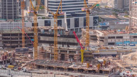 Téléchargez les photos : Grand chantier de construction avec de nombreuses grues de travail timelapse. Vue aérienne du grand développement du quartier résidentiel et de bureaux à Business Bay, Dubaï. Travailleurs en uniforme sur un renfort - en image libre de droit