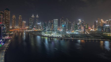 Téléchargez les photos : Panorama montrant une vue aérienne sur Dubai Business Bay et le centre-ville avec les différents gratte-ciel et tours le long du front de mer sur le canal timelapse de nuit. Site de construction avec grues - en image libre de droit