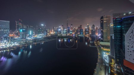 Photo for Aerial panoramic view to Dubai Business Bay and Downtown with the various skyscrapers and towers along waterfront on canal night timelapse during all night. Construction site with cranes - Royalty Free Image