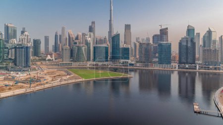 Téléchargez les photos : Vue aérienne vers Dubai Business Bay et Downtown au lever du soleil avec les différents gratte-ciel et tours le long du front de mer sur le canal timelapse. Site de construction avec grues. Soleil réfléchi par le verre - en image libre de droit