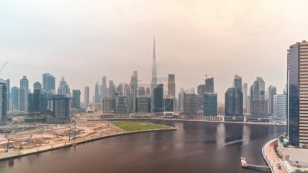 Foto de Vista panorámica aérea de Dubai Business Bay y el centro de la ciudad con los diversos rascacielos y torres a lo largo de la costa en el timelapse canal durante todo el día. Planta de construcción con grúas. Cielo nublado - Imagen libre de derechos