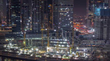 Foto de Gran obra de construcción con muchas grúas de trabajo timelapse noche. Vista aérea superior de gran desarrollo del distrito residencial y de oficinas en Business Bay, Dubai. Luces en torres iluminadas y tráfico - Imagen libre de derechos