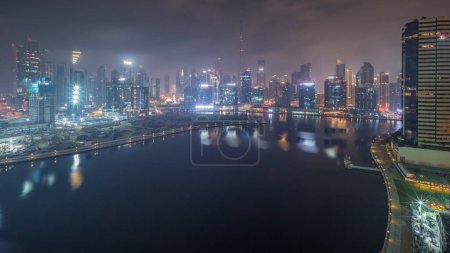 Foto de Vista panorámica aérea de Dubai Business Bay y el centro con varios rascacielos y torres a lo largo de la costa en la noche del canal timelapse durante toda la noche. Planta de construcción con grúas. Luces intermitentes - Imagen libre de derechos