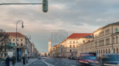 Téléchargez les photos : Ludwigstrasse et l'église Saint-Ludwig vu de Odeonsplatz timelapse. Trafic à l'intersection avec de nombreuses voitures et bus pendant le coucher du soleil. Munich, Allemagne - en image libre de droit