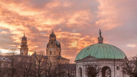 Der Diana-Pavillon-Tempel mit Bayern-Statue in der Mitte des Hofgarten-Residenzgartens in München im Zeitraffer bei Sonnenuntergang. Im Hintergrund die barocke Theatinerkirche. Deutschland
