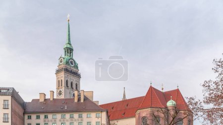 Der Glockenturm der Peterskirche am Viktualienmarkt in München. Historische Häuser mit roten Dächern. Bewölkter Himmel