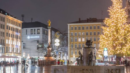 Foto de Fish Fountain, Fischbrunnen en frente del New New Town Hall en Marienplatz night timelapse, la plaza del centro histórico iluminada durante la noche de lluvia en Munich, Alemania - Imagen libre de derechos