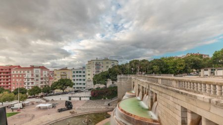 Téléchargez les photos : Panorama montrant la vue aérienne de Jardim da Alameda à Lisbonne avec la fontaine lumineuse (Fonte Luminosa) timelapse pendant le coucher du soleil. Nuages dramatiques sur les maisons colorées autour de la place avec pelouse verte - en image libre de droit