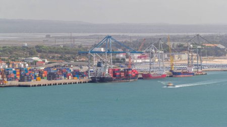 Photo for Aerial view of various containers stored in the container terminal near water timelapse, Setubal, Portugal. Cranes loading and unloading cargo ships. Boats passing by - Royalty Free Image
