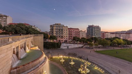 Téléchargez les photos : Panorama montrant la pelouse à Alameda Dom Afonso Henriques avec des bâtiments colorés et illuminés Fontaine lumineuse transition aérienne jour-nuit timelapse d'en haut après le coucher du soleil à Lisbonne, Portugal - en image libre de droit