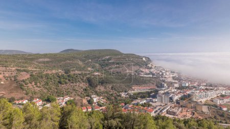 Panorama showing aerial View of Sesimbra Town and Port covered by fog timelapse, Portugal. Top landscape above the clouds from castle viewpoint. Resort in Setubal district
