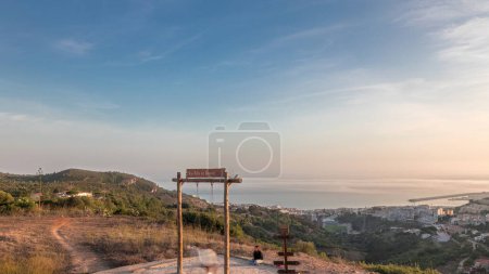 Panorama mit Luftaufnahme der Stadt Sesimbra und des Hafens im Zeitraffer bei Sonnenuntergang, Portugal. Top Abendlandschaft mit Burg auf dem Hügel vom Aussichtspunkt mit Schaukel. Resort im Distrikt Setubal