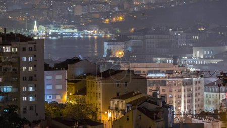 Photo for Aerial view of Lisboa downtown night timelapse. Panoramic of Baixa, Rossio and Chiado rooftops from above. Illuminated buildings. Almada on the other side of Tejo river. Portugal - Royalty Free Image