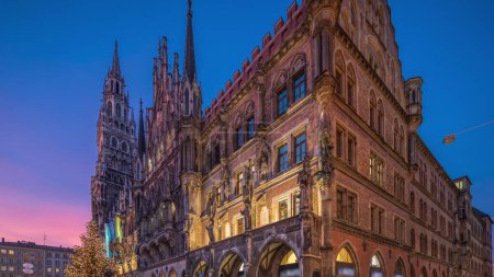Main facade of the New Town Hall (Neues Rathaus) building at the northern part of Marienplatz day to night transition timelapse in Munich after sunset. Fischbrunnen fountain in front. Bavaria, Germany.