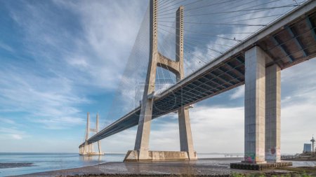 Foto de Vasco da Gama puente timelapse hiperlapso con reflexión sobre el agua y el cielo azul nublado. Puente de cable y río Tajo. Lisboa, Portugal. - Imagen libre de derechos