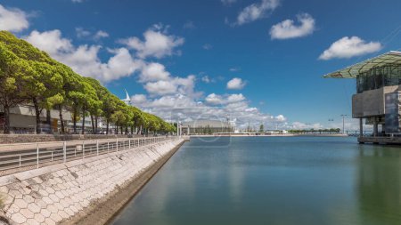 Panorama showing Lisbon Oceanarium timelapse, located in the Park of Nations or Parque das Nacoes. The largest indoor aquarium in Europe. Waterfront with green trees and clouds on a blue sky. Portugal