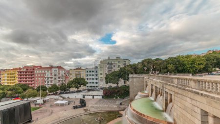 Foto de Panorama que muestra la vista aérea de Jardim da Alameda en Lisboa con la fuente luminosa (Fonte Luminosa) timelapse durante la puesta del sol. Dramáticas nubes sobre coloridas casas alrededor de la plaza con césped verde - Imagen libre de derechos