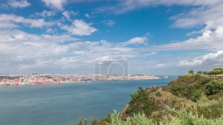 Panorama showing Lisbon cityscape and Tagus river timelapse, aerial view of Old Town Alfama with landmark suspension 25 of April bridge from viewpoint of Cristo Rei in Almada. Portugal