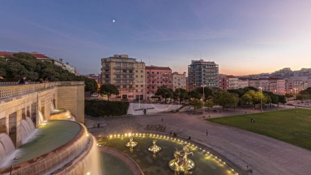 Panorama mit Rasen am Alameda Dom Afonso Henriques mit bunten Gebäuden und beleuchtetem Luminous Fountain Tag-Nacht-Übergang von oben nach Sonnenuntergang in Lissabon, Portugal