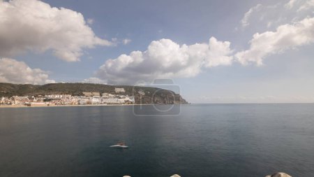 Téléchargez les photos : Panorama avec vue sur la ville de Sesimbra et Port Timelapse, Portugal. Paysage Skyline avec bateaux, maisons et plage depuis le phare sur une jetée. Resort dans le quartier de Setubal. De beaux nuages - en image libre de droit