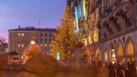 Foto de Fuente de pescado, Fischbrunnen en frente del nuevo ayuntamiento en Marienplatz día a noche timelapse transición, la plaza del centro histórico iluminado después de la puesta del sol en Munich, Alemania - Imagen libre de derechos
