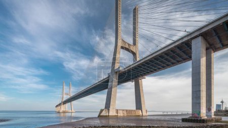 Foto de Vasco da Gama puente timelapse hiperlapso con reflexión sobre el agua y el cielo azul nublado. Puente de cable y río Tajo. Lisboa, Portugal. - Imagen libre de derechos