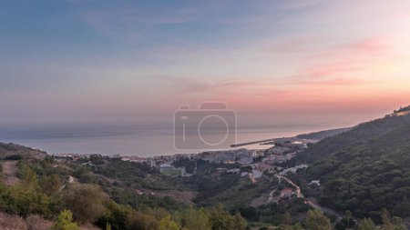 Téléchargez les photos : Panorama montrant la vue aérienne de la ville de Sesimbra et du port de jour à la nuit timelapse de transition, Portugal. Paysage du soir avec château sur la colline d'en haut. Resort dans le quartier de Setubal - en image libre de droit