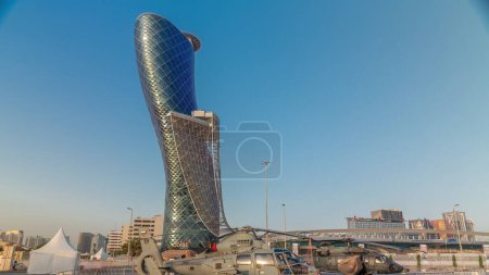 Téléchargez les photos : Abu Dhabi, Émirats arabes unis - 25 février 2023 : Centre national des expositions (ADNEC) où s'est tenue l'exposition militaire IDEX au coucher du soleil. Vue extérieure avec des reflets solaires gratte-ciel moderne derrière les hélicoptères - en image libre de droit