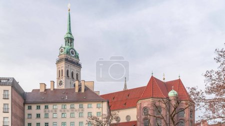 St. Peter's Church Peterskirche clock tower along Viktualienmarkt market street timelapse in Munich, Bavaria, Germany. Historic houses with red roofs. Cloudy sky