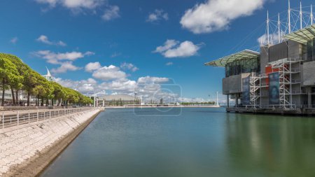 Panorama showing Lisbon Oceanarium timelapse, located in the Park of Nations or Parque das Nacoes. The largest indoor aquarium in Europe. Waterfront with green trees and clouds on a blue sky. Portugal