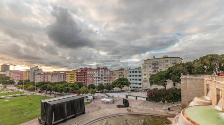 Téléchargez les photos : Panorama montrant la vue aérienne de Jardim da Alameda à Lisbonne avec la fontaine lumineuse (Fonte Luminosa) timelapse pendant le coucher du soleil. Nuages dramatiques sur les maisons colorées autour de la place avec pelouse verte - en image libre de droit