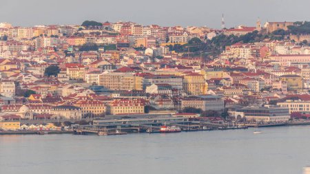 Téléchargez les photos : Vue aérienne du terminal de ferry de Cais Do Sodre par la rivière Tage avec des bateaux passant par le timelapse à Lisbonne, Portugal. Maisons colorées sur un fond. Vue de dessus depuis le point de vue Cristo Rei pendant le coucher du soleil - en image libre de droit
