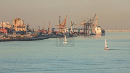 Photo for Container cargo ship during docking at industrial port with cranes aerial timelapse. Import export commercial trade business logistic and transportation. Tejo river during sunset in Lisbon, Portugal - Royalty Free Image