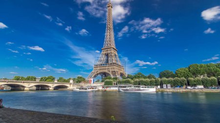 Téléchargez les photos : L'hyperlapsus intemporel de la tour Eiffel depuis le front de mer sur la Seine à Paris. Navire et bateaux sur la rivière à la journée ensoleillée d'été avec des nuages sur un ciel bleu - en image libre de droit