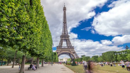 Téléchargez les photos : Champ de Mars et la Tour Eiffel intemporel hyperlapsus par une journée ensoleillée d'été. Paris, France. Des arbres verts et un ciel nuageux, des gens qui se promènent. Mouvement vers - en image libre de droit