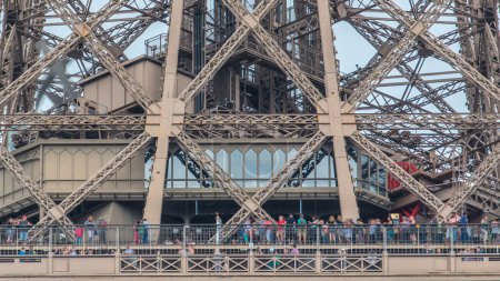 Téléchargez les photos : Vue rapprochée de la première section de la Tour Eiffel avec des touristes sur la terrasse d'observation regardant l'horizon de la ville timelapse à Paris, France. Journée d'été avec ciel nuageux bleu. - en image libre de droit