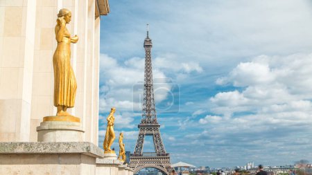 Photo for Eiffel Tower and the golden statues of women in the sun light timelapse, Trocadero square, Paris, France. Blue cloudy sky at sunny summer day - Royalty Free Image