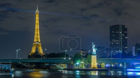 Téléchargez les photos : Petite Statue de la Liberté située près de la tour Eiffel timelapse nocturne. Pont Grenelle sur fond et bâtiments modernes. Paris, France - en image libre de droit