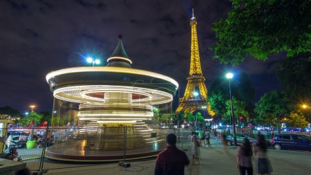 Téléchargez les photos : Carrousel vintage illuminé près de la Tour Eiffel timelapse nocturne, Paris. Personnes se promenant autour de l'attraction dans le parc - en image libre de droit