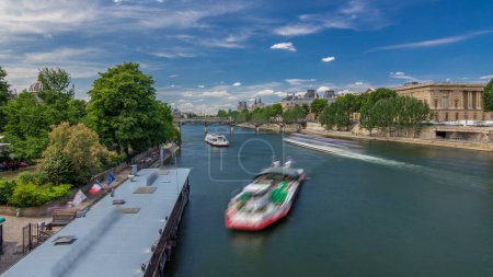 Foto de Barco turístico pasa por debajo de Pont des Arts y se detiene en una estación de barco en el río Sena timelapse hiperlapso en París. Destino turístico más importante de Europa. Cielo azul del claustro en el día de verano - Imagen libre de derechos