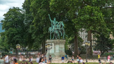 Téléchargez les photos : Statue Charlemagne et ses Leudes timelapse par Cathédrale Notre Dame de Paris. Les gens marchent et s'assoient dans le parc le jour d'été. Arbres verts sur fond - en image libre de droit