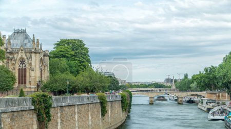 Foto de Jardín de Notre Dame de Paris en Cite Island timelapse, París, Francia. Parque con árboles verdes y flores. Vista desde el puente doble. Río con barcos flotantes. Cielo nublado en el día de verano - Imagen libre de derechos