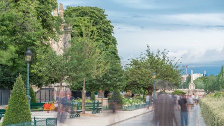 Foto de Jardín de Notre Dame de Paris en Cite Island timelapse, París, Francia. Gente caminando por el parque con árboles verdes y flores. Cielo nublado en el día de verano - Imagen libre de derechos