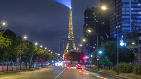Photo for Eiffel Tower and street lights at night with car light trails on the road timelapse in Paris. View from Javel with green trees - Royalty Free Image