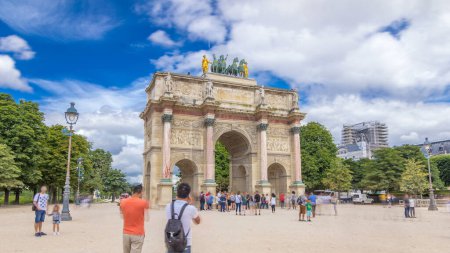 Téléchargez les photos : Arc de Triomphe (Arc de Triomphe du Carrousel) hyperlapsus intemporel dans les jardins des Tuileries à Paris, France. Touriste se promenant le jour d'été avec un ciel nuageux bleu. Statues sur le dessus - en image libre de droit