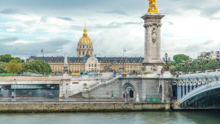 Téléchargez les photos : Trafic devant les Invalides timelapse à Paris, France. Pont d'Alexandre III qui enjambe la Seine. Nuages le jour d'été. Drapeau français au sommet - en image libre de droit