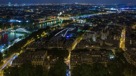 Aerial Night timelapse view of Paris City and Seine river with bridges shot on the top of Eiffel Tower observation deck. Evening illumination. Traffic on roads