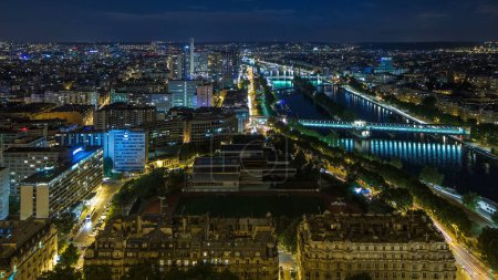 Téléchargez les photos : Vue aérienne de la ville de Paris et de la Seine de nuit prise sur le pont d'observation de la Tour Eiffel. Illumination du soir. Circulation sur les routes près du front de mer - en image libre de droit