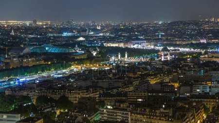 Foto de Vista del timelapse nocturno aéreo de la ciudad de París y el río Sena en la parte superior de la plataforma de observación de la Torre Eiffel. Iluminación vespertina del Puente de Alejandro III - Imagen libre de derechos